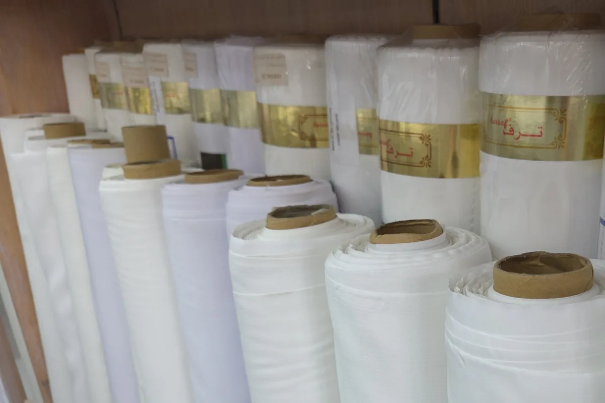 White fabric rolls on a wooden shelf with gold labels