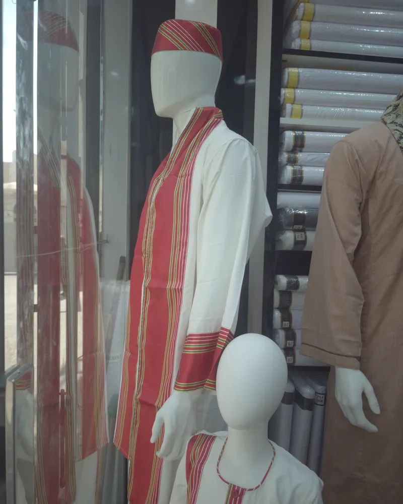 A mannequin in the white Sudanese groom’s thobe with a red striped shawl, and the child’s set beside it