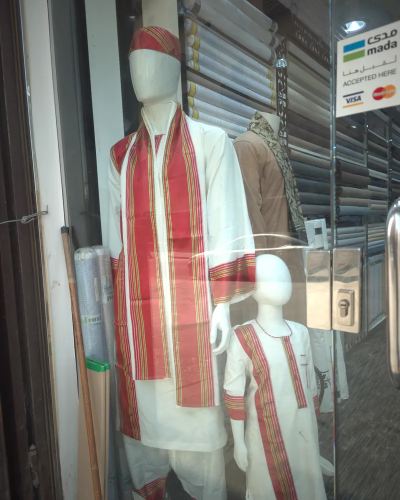 A mannequin in the white Sudanese groom’s set with a red striped shawl, and a child mannequin in the same set beside it