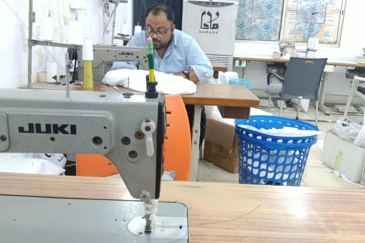 A tailor stitching a white thobe on a sewing machine in the Ramada Al-Raqi Tailoring workshop