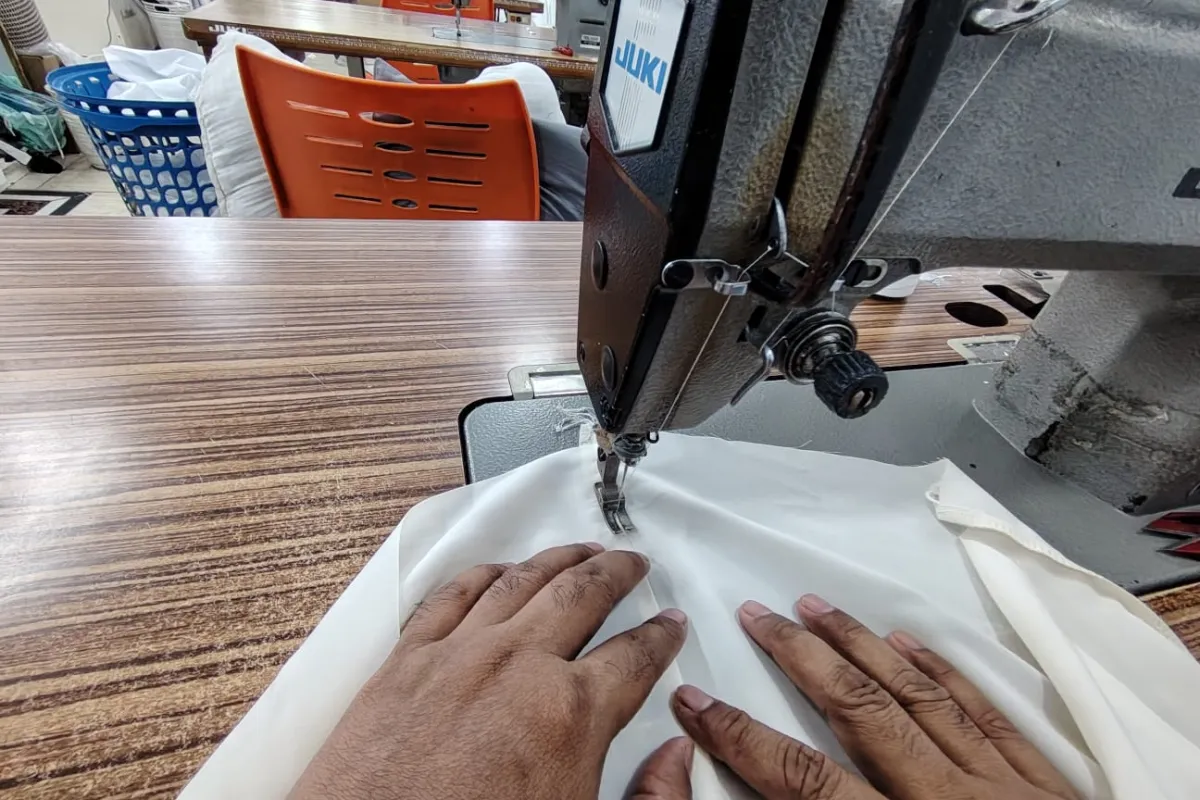 A tailor’s hands guiding thobe fabric through the sewing machine at Ramada Al-Raqi Tailoring